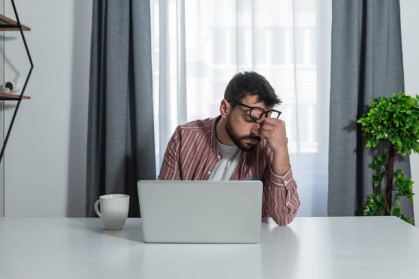 computer programmer looking sad with a laptop on the table in front of him