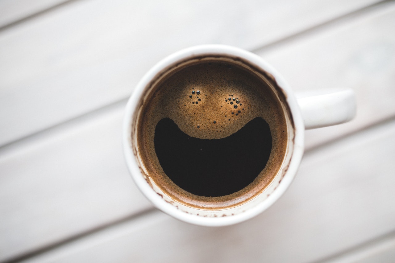 A cup of coffee seen from above, with bubbles making a smiley face.
