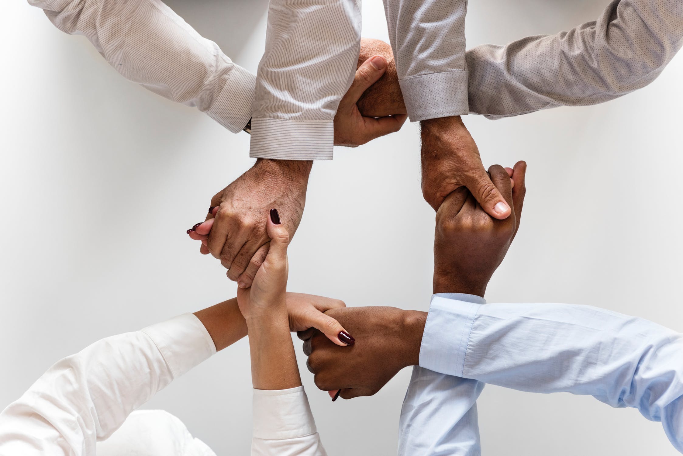 Four people's arms, all holding hands with each other to form a cross shape.