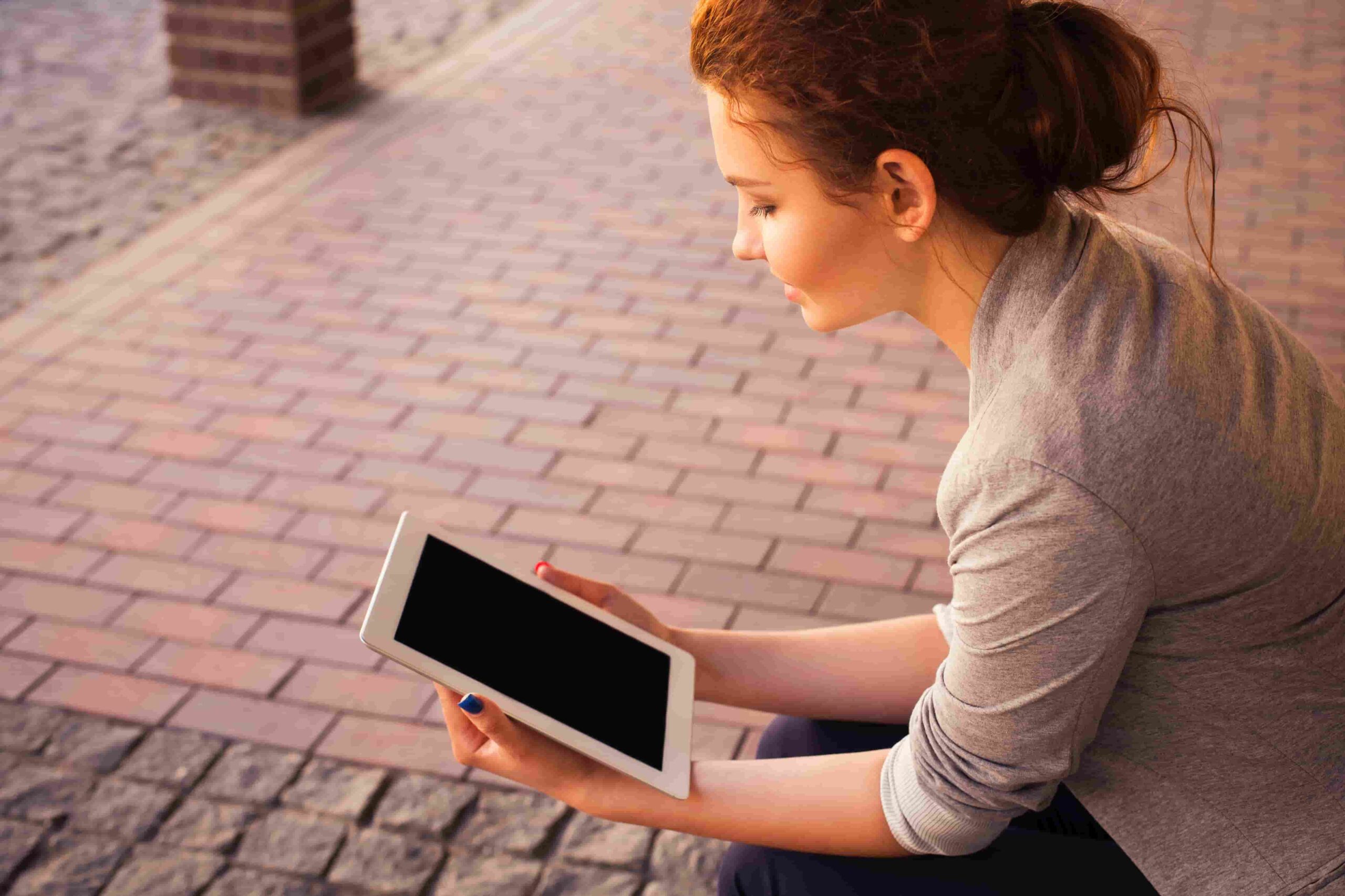 Someone sitting and looking at a turned-off tablet.